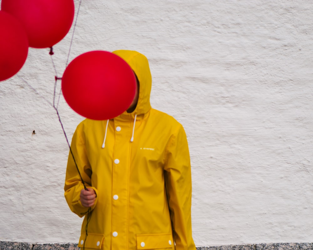 uma pessoa em uma capa de chuva amarela segurando balões