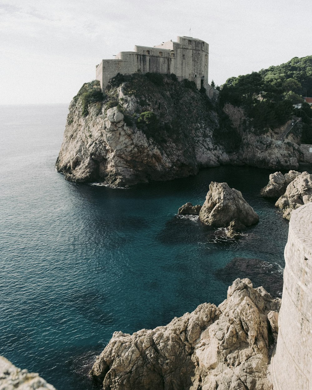 a stone building on a cliff over the ocean with Lovrijenac in the background