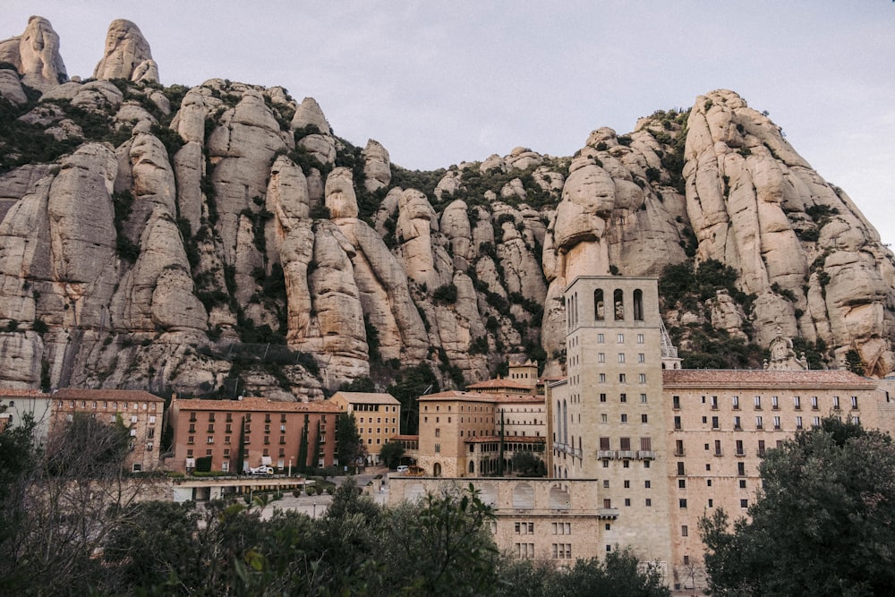 un gran edificio con una gran formación rocosa detrás con Montserrat al fondo