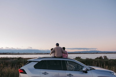 a man and a woman sitting on a car in a field