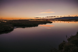 a body of water with trees and a sunset in the background
