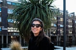 A smiling woman wearing oversized, stylish sunglasses on a sunny city street.