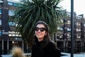 A smiling woman wearing oversized, stylish sunglasses on a sunny city street.