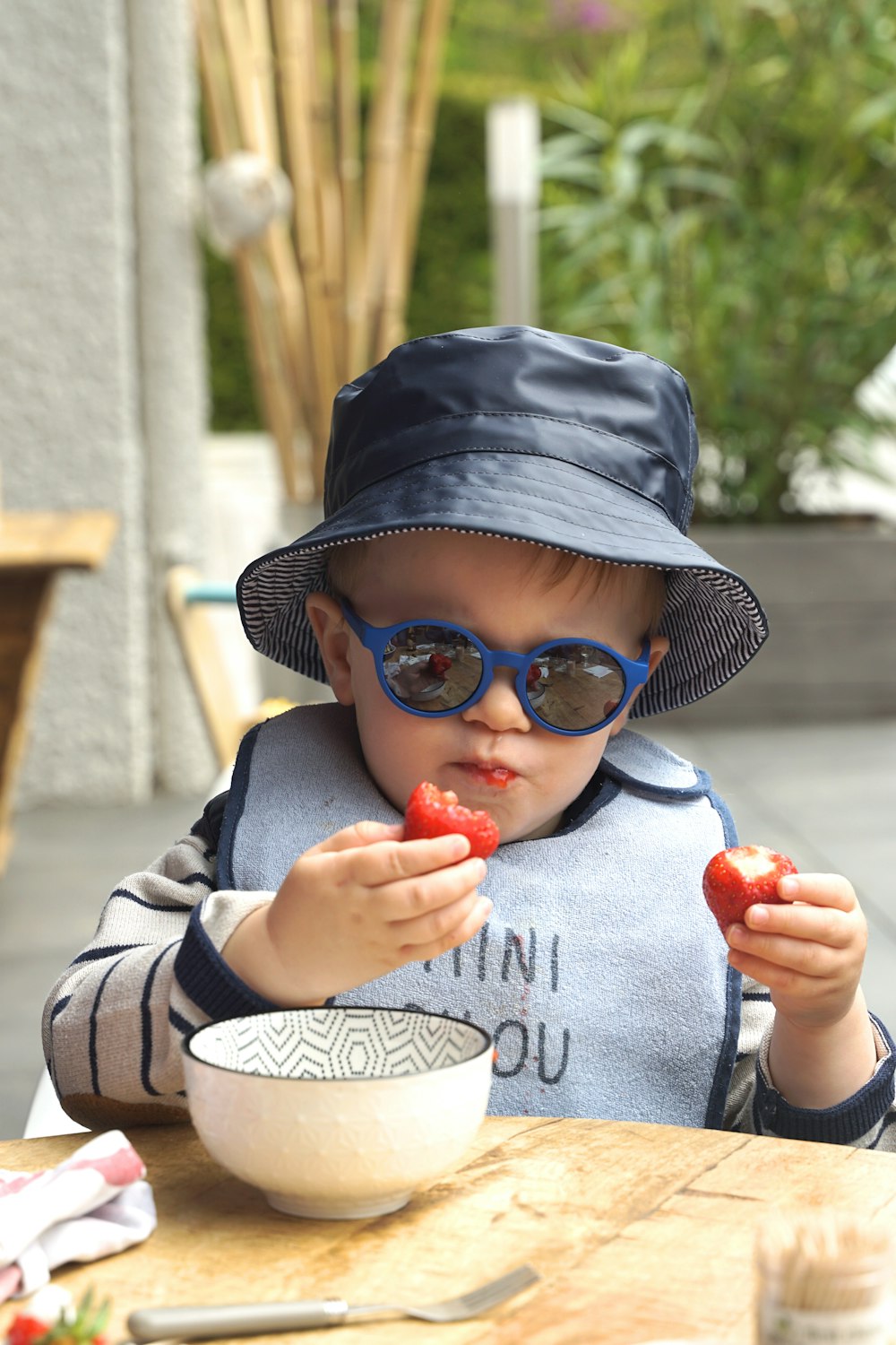 サングラスをかけ、帽子をかぶった赤ちゃんがイチゴを食べる