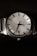 A classic wristwatch with a metallic band and a round face, featuring a detailed textured dial with black hour markers. The hands are sleek and the watch displays the date on the dial.