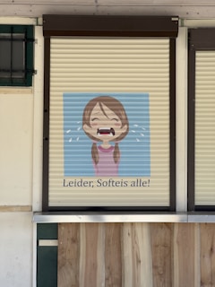 A rolling shutter with a cartoon image of a crying girl depicted on it. Below the image, there is German text that reads 'Leider, Softeis alle!' suggesting that soft serve ice cream is sold out.
