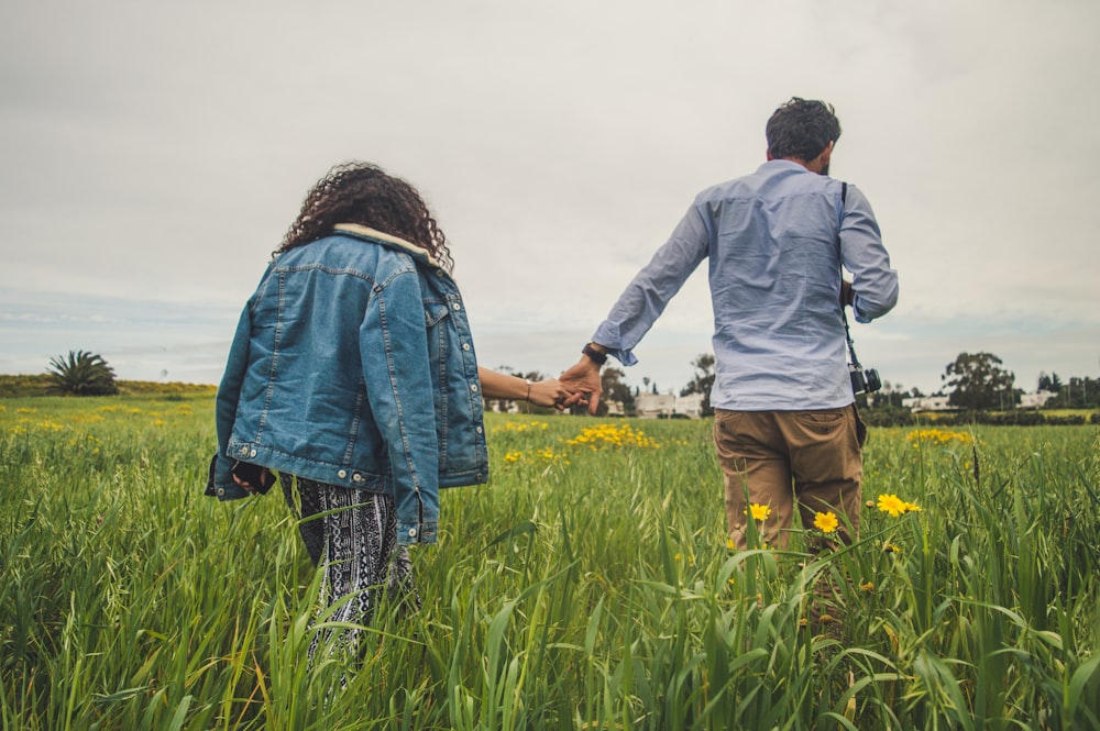 a man and woman holding hands in a field of grass