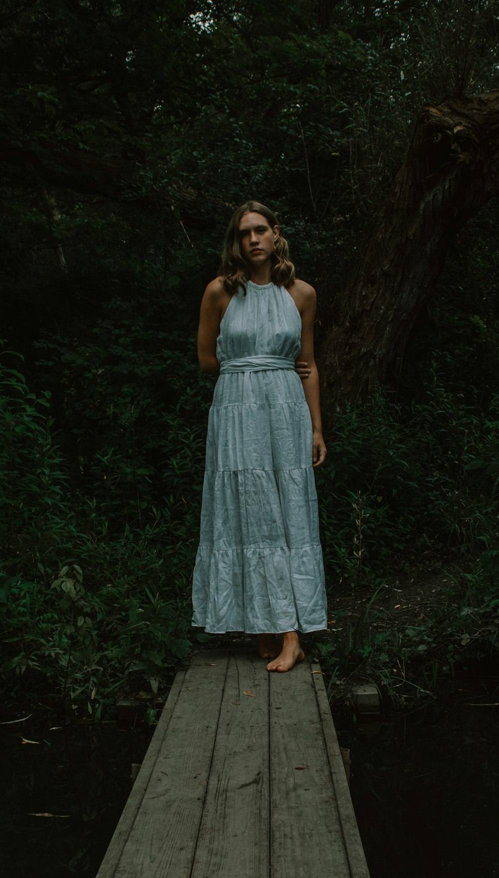 a person in a dress standing on a wooden platform in the woods