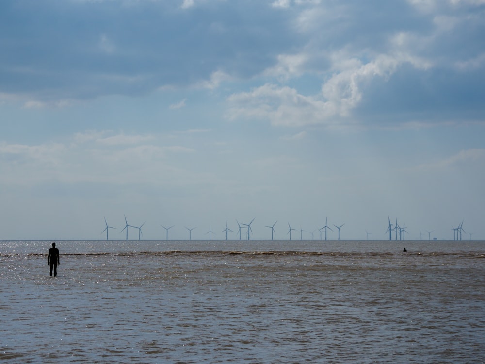 a person standing in a body of water with wind turbines in the background