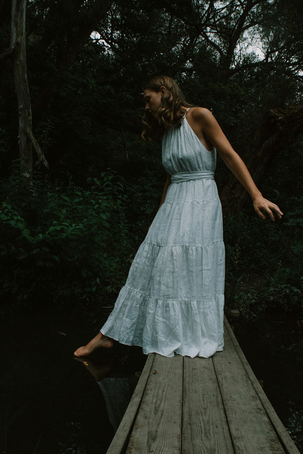 a person in a dress sitting on a wooden bench in the woods