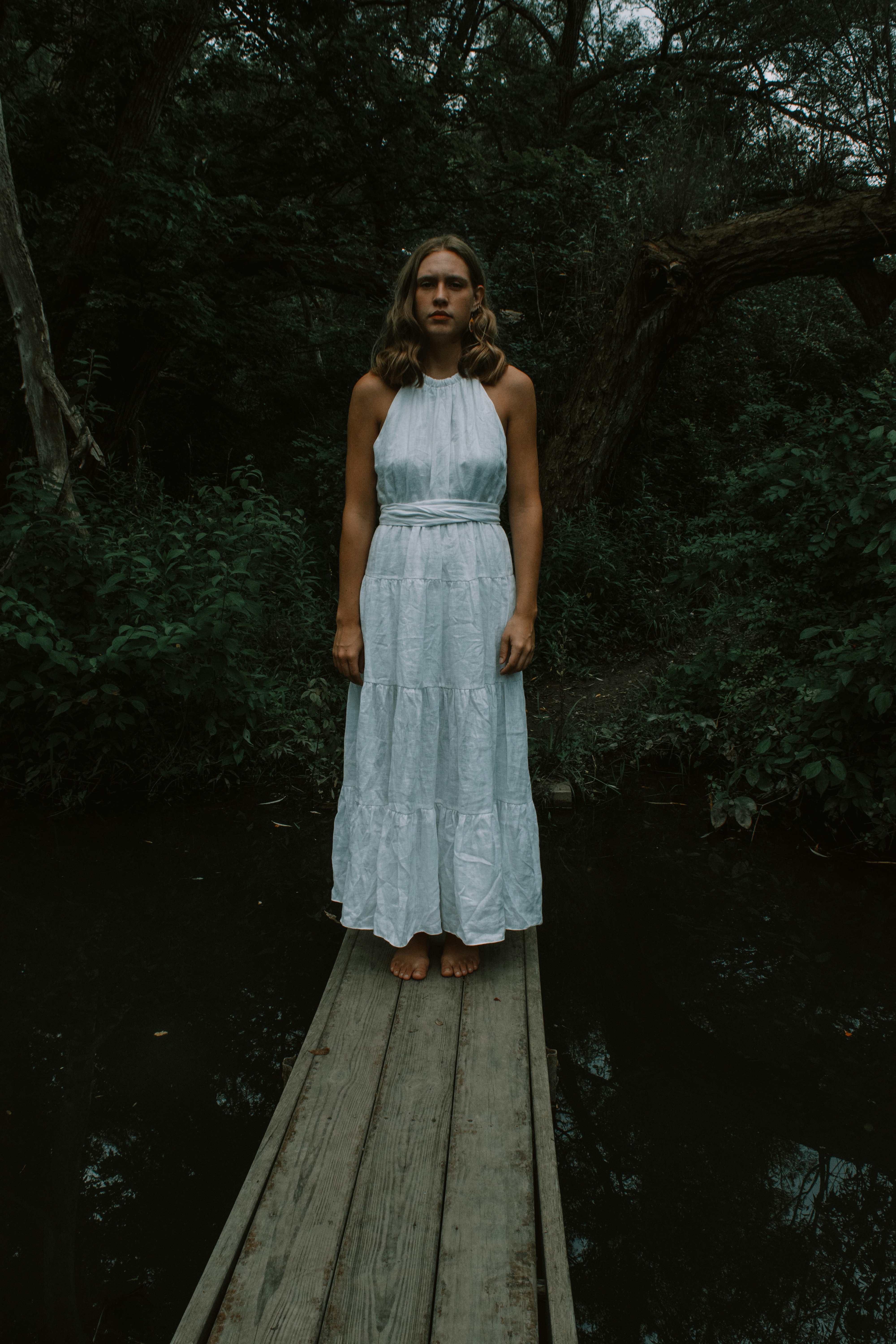 a person in a white dress standing on a wooden platform in a forest
