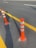 Several orange and white traffic delineator posts are arranged alongside freshly painted yellow lines on an asphalt road. The long shadows suggest it is either early morning or late afternoon.