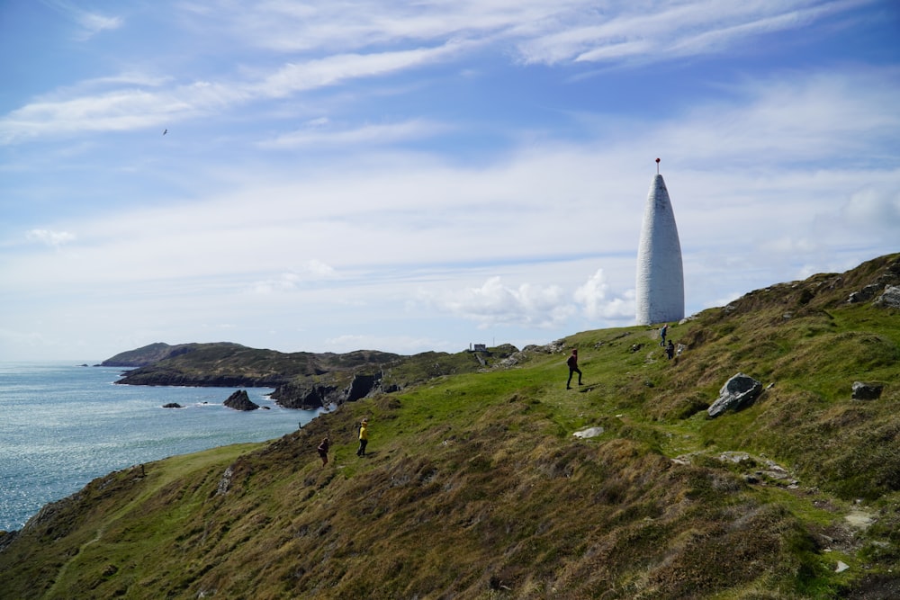 a tall white tower on a hill by the ocean