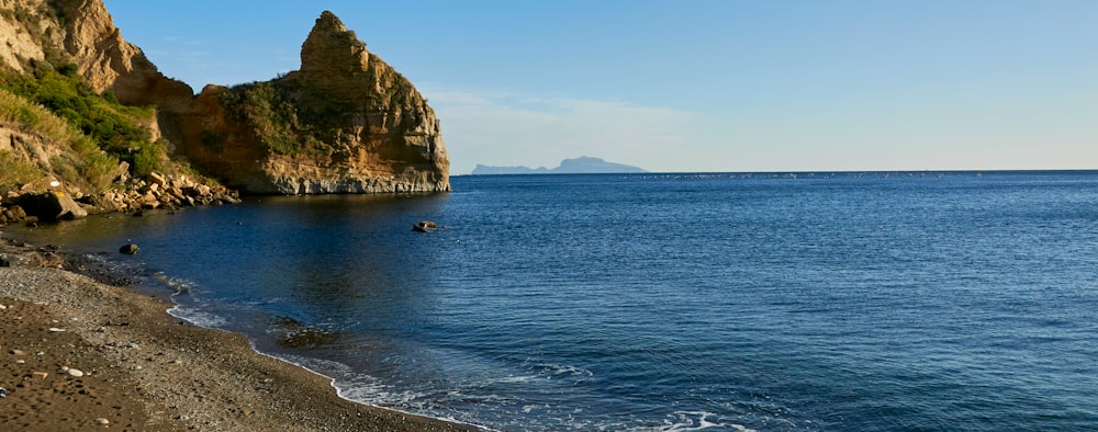 a body of water with a rocky shoreline and a beach with a blue sky