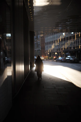 A candid shot of Rina walking through a quiet city street at dusk, her silhouette blending with minimalist urban architecture.
