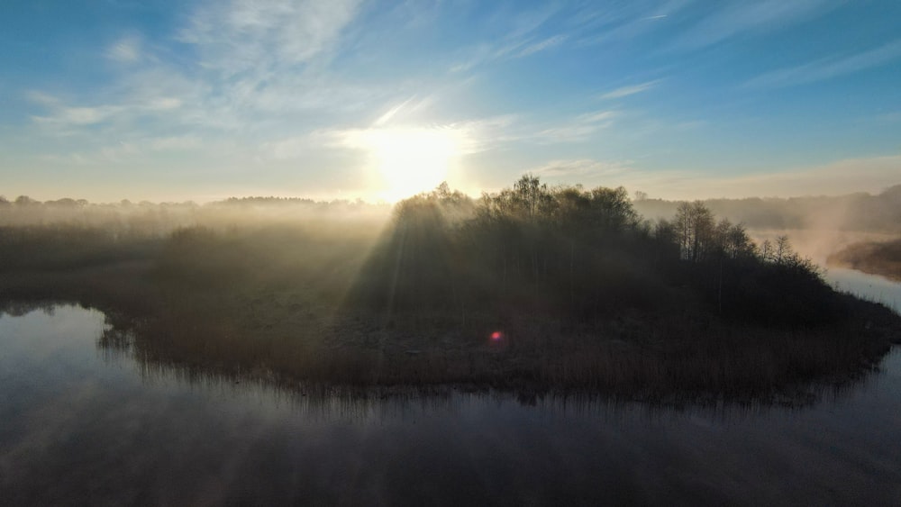 a body of water with trees and the sun in the background