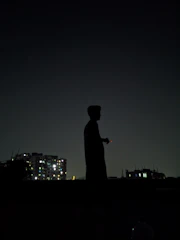 Silhouette of a lone man standing against a dark urban backdrop at night.