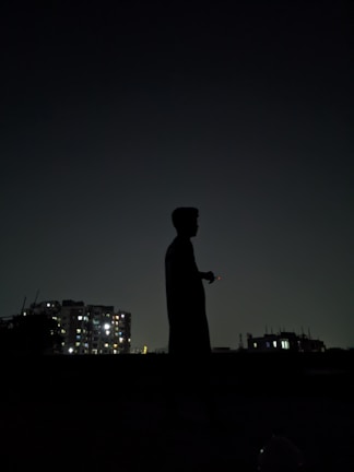 A shadowed figure stands against a backdrop of towering neon-lit skyscrapers under a dark, stormy sky.