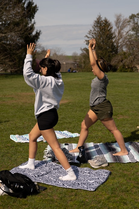 a couple of girls stretching on a blanket in a grassy field