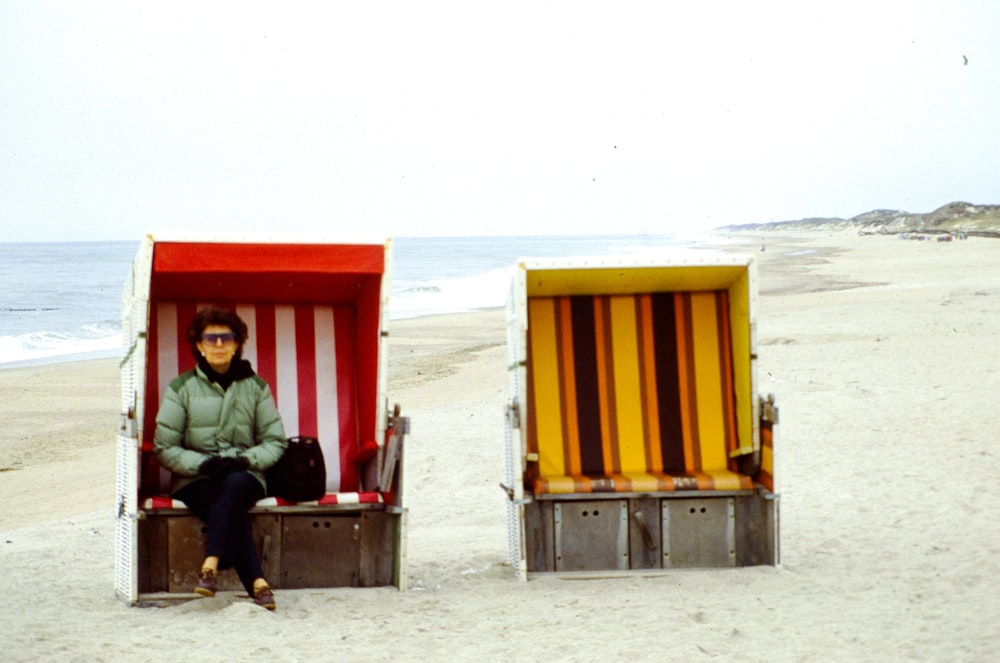 a person sitting in a chair next to a small yellow building on a beach