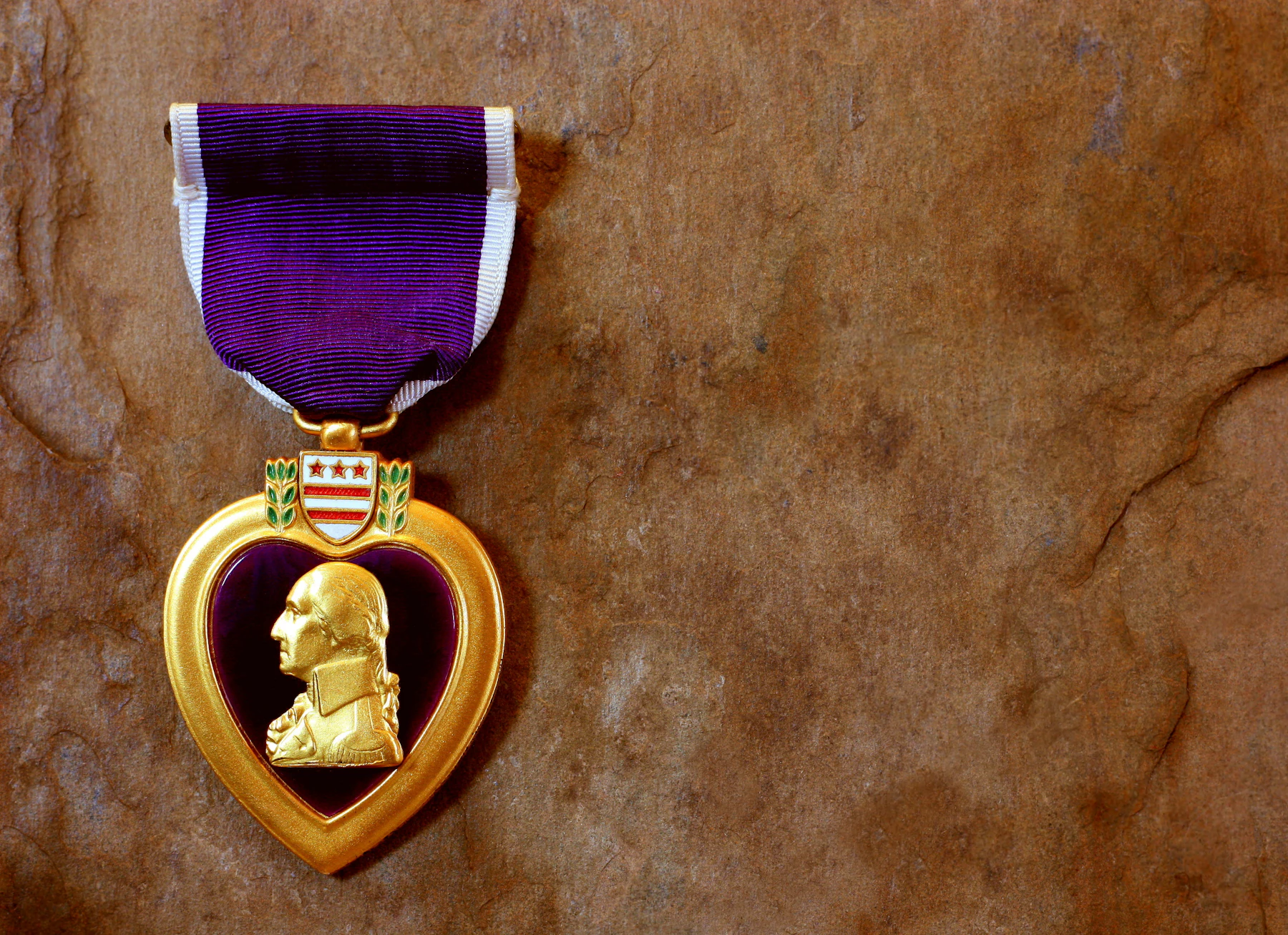 A purple heart medal on its purple ribbon lying on brown stone