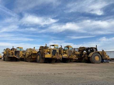 A fleet of dump trucks and heavy equipment lined up ready for transport on a sunny day.