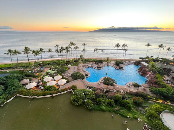 Luxurious beachfront resort at sunset with elegant pool and palm trees.