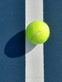 Close-up of a tennis ball resting on a vibrant neon-yellow tennis court surface.