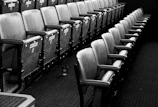 Light airy photo of empty wooden theater seats with white wall.