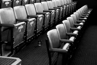 Light airy photo of empty wooden theater seats with white wall.