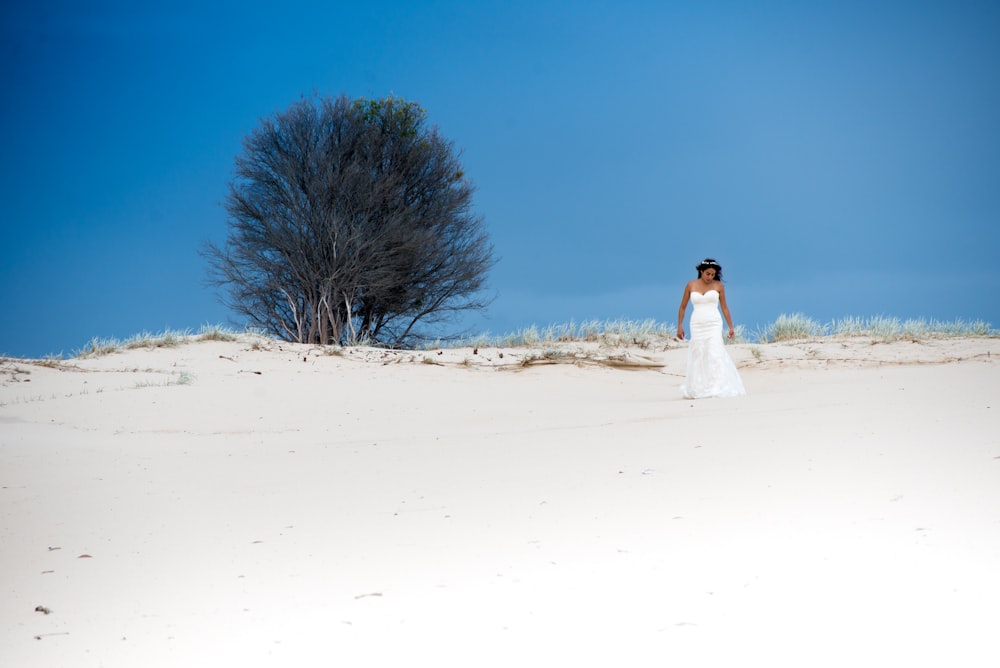 a man in a white dress walking in the sand