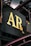A close-up view of a metal signboard with large, gold-colored letters 'AR Co.' against a dark background. The sign is part of an industrial structure with visible metal beams and pipes surrounding it.