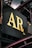 A close-up view of a metal signboard with large, gold-colored letters 'AR Co.' against a dark background. The sign is part of an industrial structure with visible metal beams and pipes surrounding it.