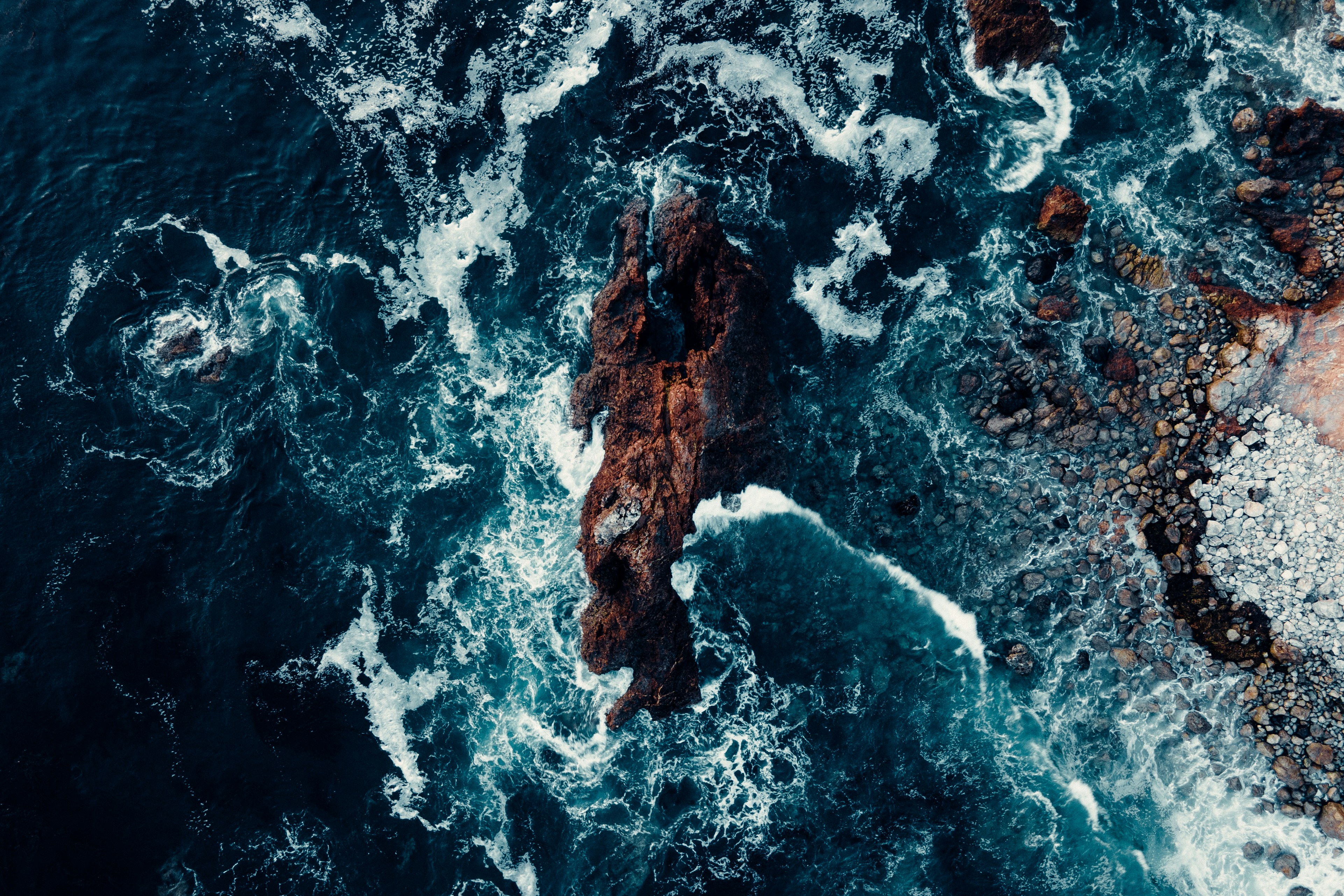 Aerial cliffside view of waves crashing on rocks in the ocean.