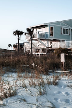 A coastal house with storm shutters and elevated foundation surrounded by palm trees.