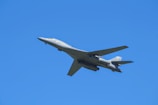 A sleek military aircraft soaring above rugged mountain terrain under clear skies.