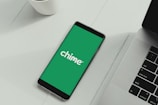 A smartphone displaying the Chime logo on a green background is placed next to a laptop on a white surface.
