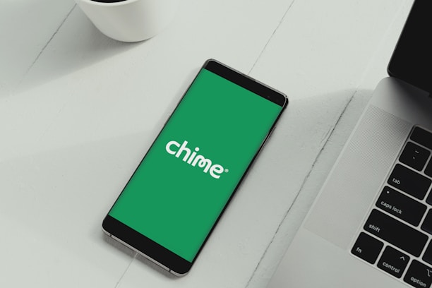 A smartphone displaying the Chime logo on a green background is placed next to a laptop on a white surface.