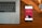 A wooden desk hosts a laptop on the left and a smartphone on the right, which displays an advertisement for a bank with the slogan 'Spend and save smartly'. A wristwatch lies above the phone, its metallic face and band accented by the warm tones of the wood.