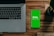 A laptop with a partially visible keyboard situated on a wooden surface next to a smartphone displaying a green screen with the word 'bisq' and the text 'Exchange, Decentralized'. There is also a small potted plant in the top-right corner.