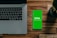 A laptop with a partially visible keyboard situated on a wooden surface next to a smartphone displaying a green screen with the word 'bisq' and the text 'Exchange, Decentralized'. There is also a small potted plant in the top-right corner.
