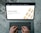 Hands typing on a laptop keyboard with an open webpage displaying information about buying precious metals such as gold, silver, platinum, and palladium. The screen shows an image of gold bars arranged in a pattern. The background consists of a wooden floor with a distressed look.