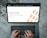 Hands typing on a laptop keyboard with an open webpage displaying information about buying precious metals such as gold, silver, platinum, and palladium. The screen shows an image of gold bars arranged in a pattern. The background consists of a wooden floor with a distressed look.