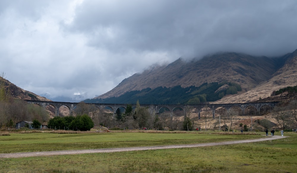 a large stone bridge over a grassy field with a mountain in the background