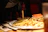 Plate with a ham sandwich and golden onion rings, served with a side of pickles.