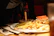 Plate with a ham sandwich and golden onion rings, served with a side of pickles.