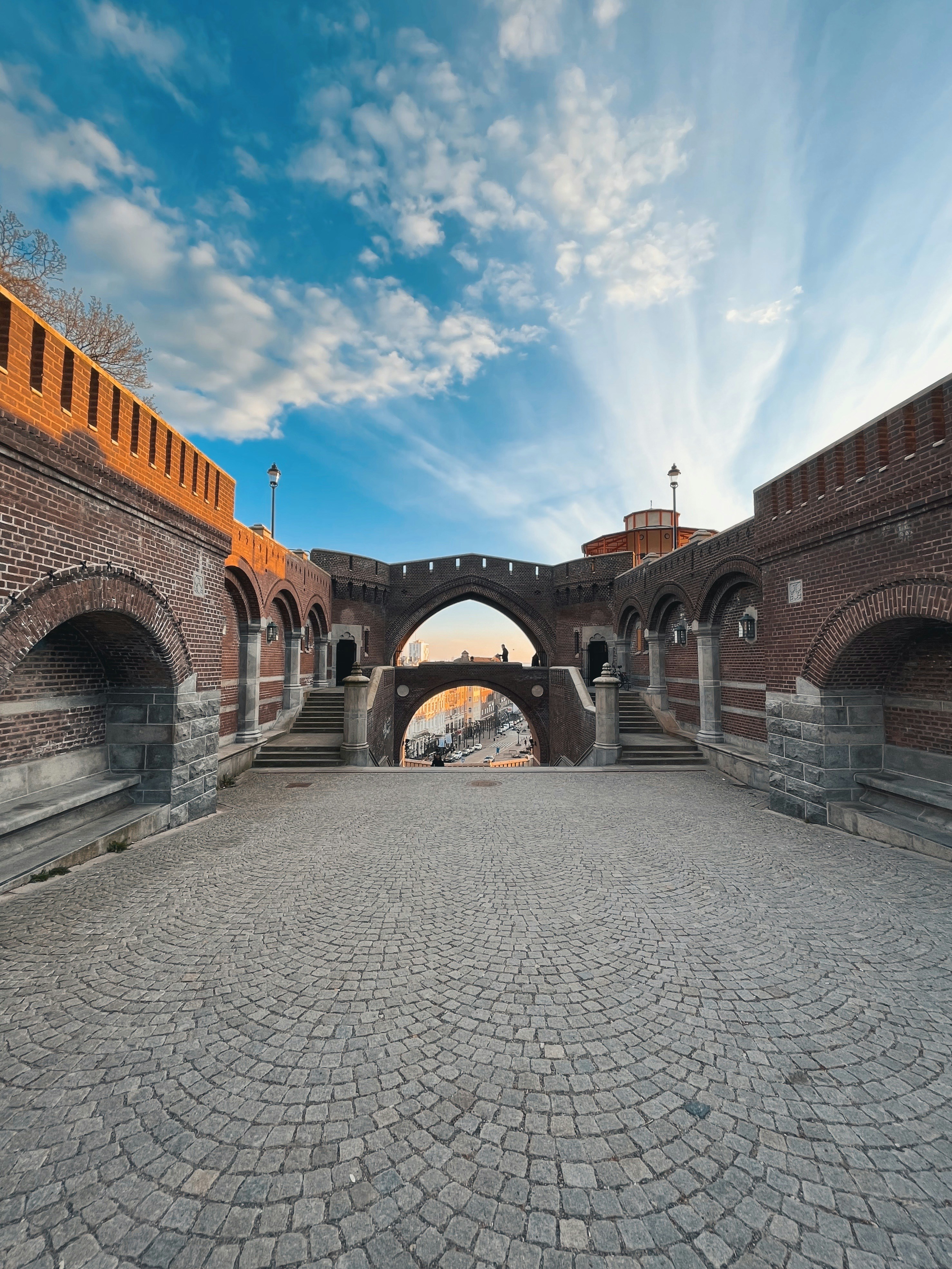 a stone walkway with a stone walkway and a stone wall with a blue sky and clouds