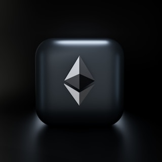 A sleek, modern design featuring a three-dimensional geometric shape resembling the Ethereum logo, centered on a glossy dark gray square with subtle lighting effects. The background fades into a deep black, highlighting the central emblem.