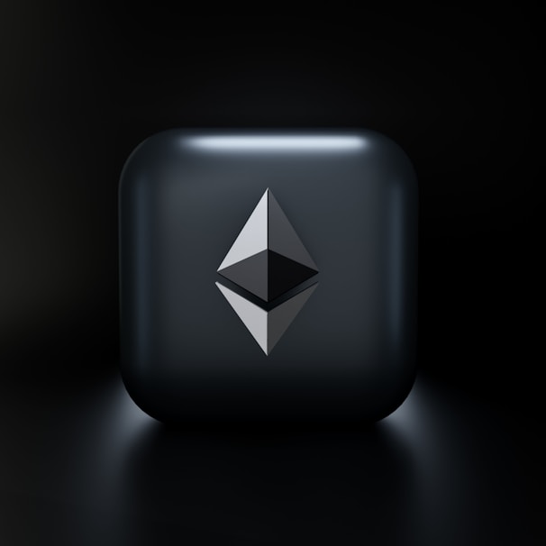 A sleek, modern design featuring a three-dimensional geometric shape resembling the Ethereum logo, centered on a glossy dark gray square with subtle lighting effects. The background fades into a deep black, highlighting the central emblem.