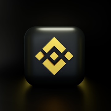 A dark, glossy black cube featuring a yellow geometric logo on its front, with a smooth reflective surface and a subtle glow around the edges.
